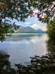 View of a lake and mountains through a gap in the trees; multi-coloured bunting strung between them