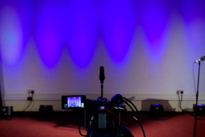 camera pointing at a microphone and blue-lit stage space